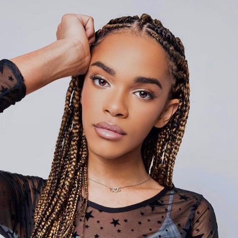 Yasmin Finney, a slim Black trans women, poses for a portrait. She has long cornrows and it wearing a black mesh long-sleeved star shirt over a light blue camisole.