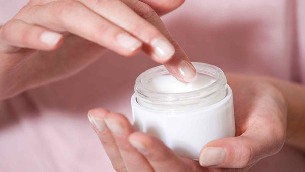 A woman's hand holding a jar of moisturizer for soothing itchy legs after shaving.