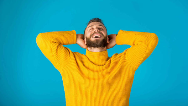 Un hombre con un suéter amarillo que experimenta alivio del cuero cabelludo con las manos en la cabeza.