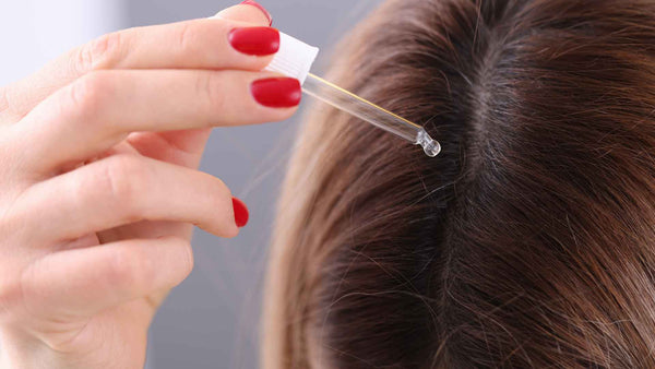 Una mujer está poniendo aceite del cuero cabelludo en su cabello.