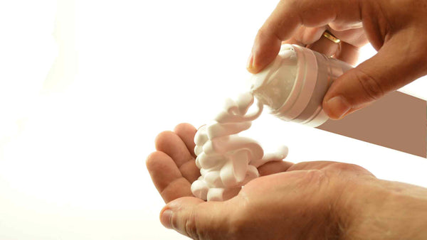 A person's hand is holding a can of shaving cream to prevent itchy legs after shaving.