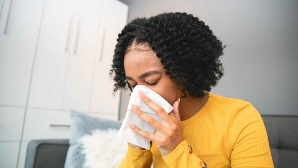Una mujer en un sofá se suena la nariz, lo que indica síntomas de alergias.