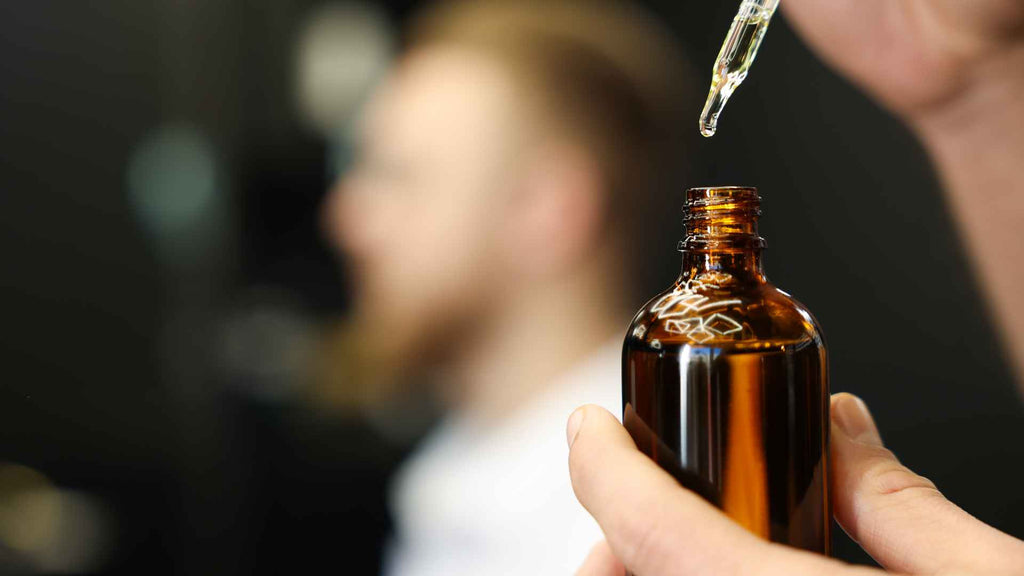 A man is pouring a beard oil into a bottle.