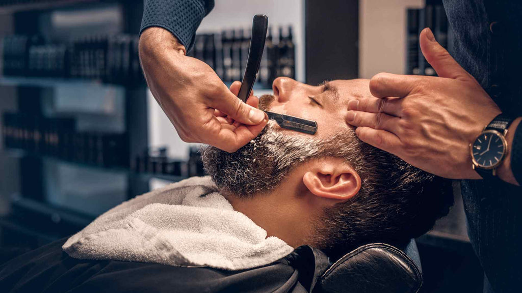 A man getting his beard shaved at a barber shop.