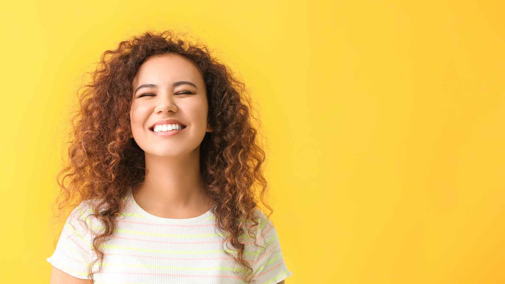 A smiling woman with curly hair against a yellow background.