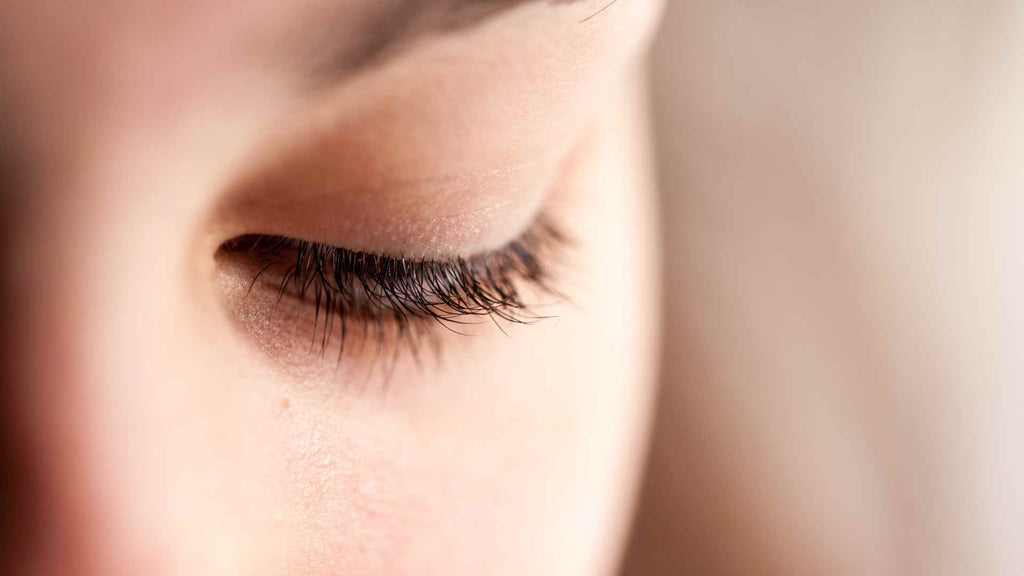 A close up of a woman's eye with long lashes experiencing eyelid itch.