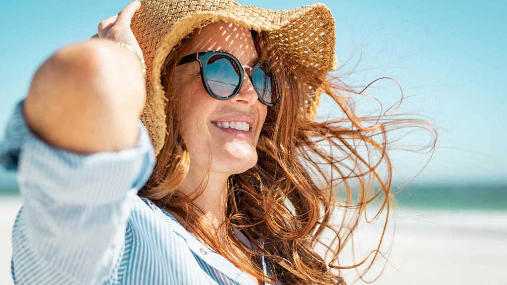 A woman wearing sunglasses and a straw hat on the beach.
