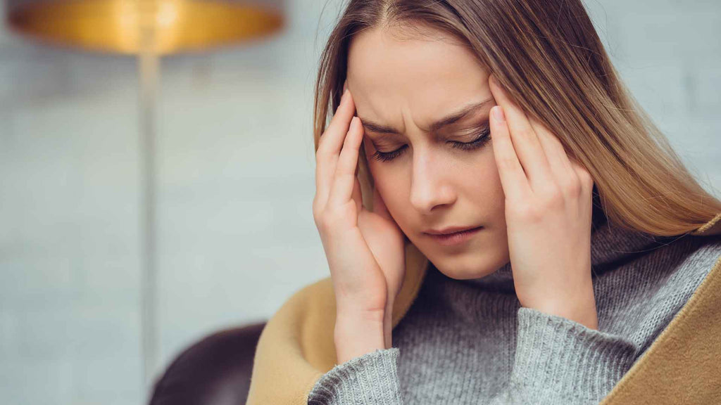 A woman is holding her head with her hands, displaying signs of a headache.