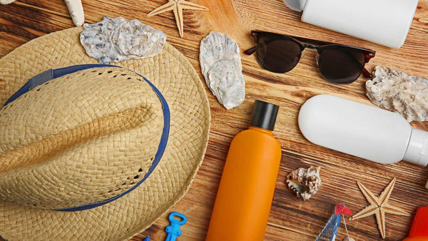 Sombrero, gafas de sol, protector solar e hidrocortisona en una mesa de madera.