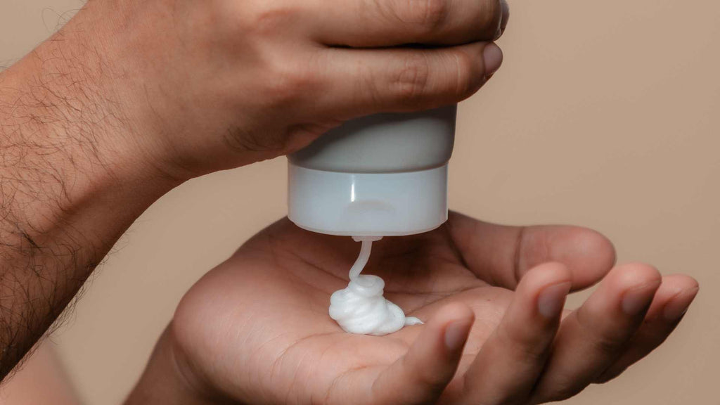 A man's hand holding a tube of hydrocortisone cream to soothe sunburn.