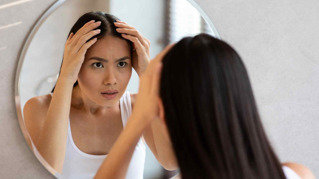 Woman examining her forehead in the mirror, showing concern for her appearance.
