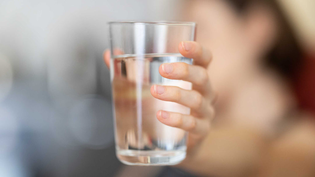 Person holding a clear glass of water toward the camera with a blurred background.