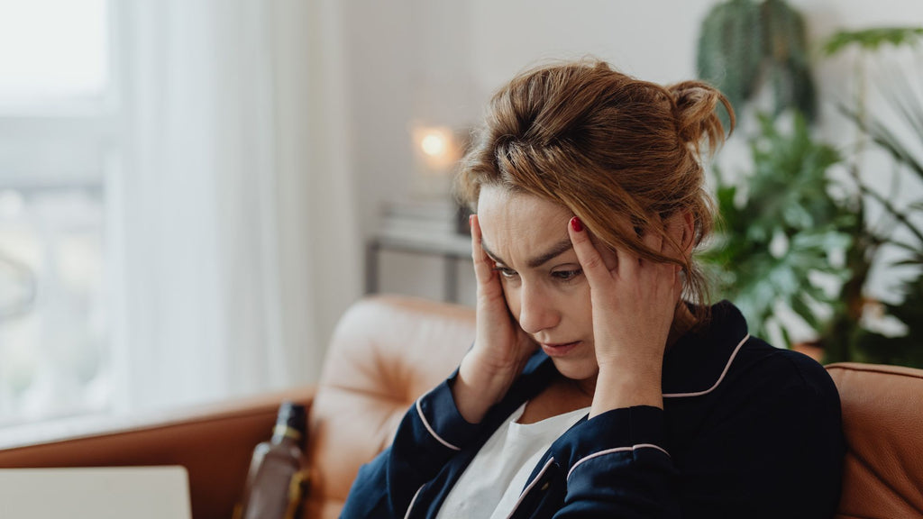 A stressed woman is sitting on a couch with her hands on her head.