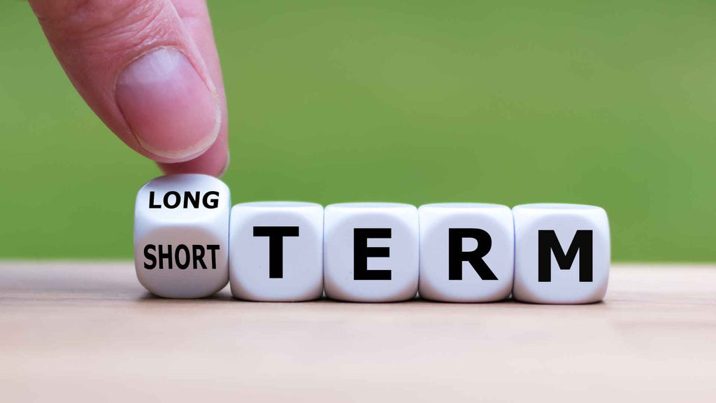 A finger flipping a cube with the word "short" to "long," creating the phrase "long term.