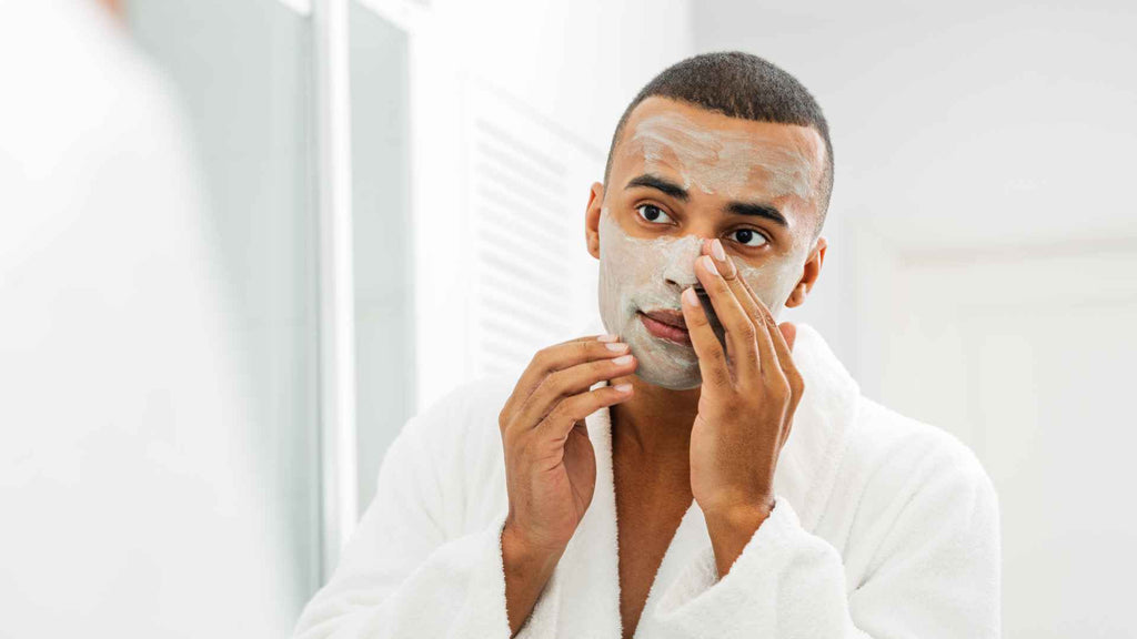A man applying facial cleanser or mask while looking into a mirror.