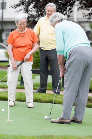 Three elderly people putting on a golf green