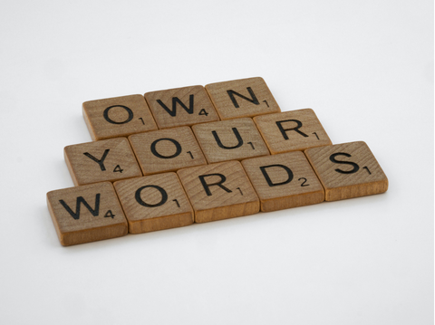 Scrabble pieces arranged to read 'Own Your Words'