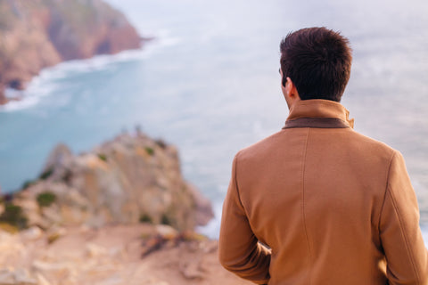a man in a woolen coat looking out to the sea