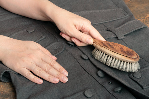 a grey wool coat being brushed gently to remove dirt