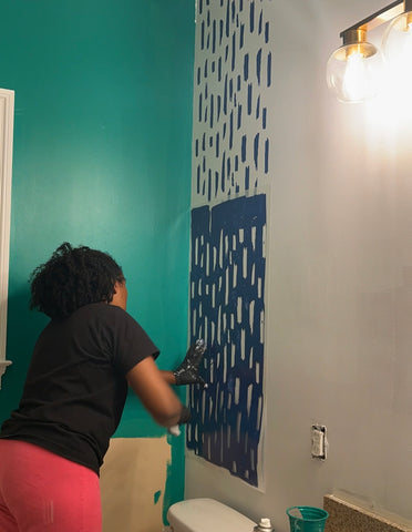 person painting a wall with a stencil pattern in blue