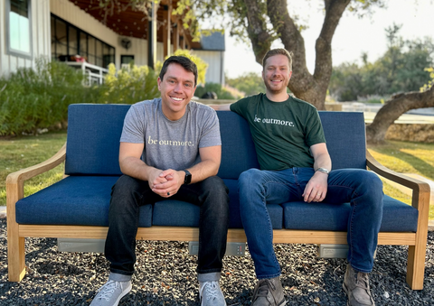 Co-Founders of Outmore Living sitting on the Solerno Heated Outdoor Sofa in front of a beautiful modern Austin Backyard scene