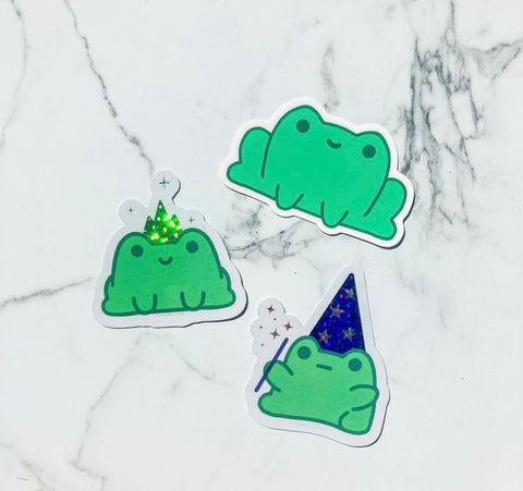 Three green frog stickers on a white marble background