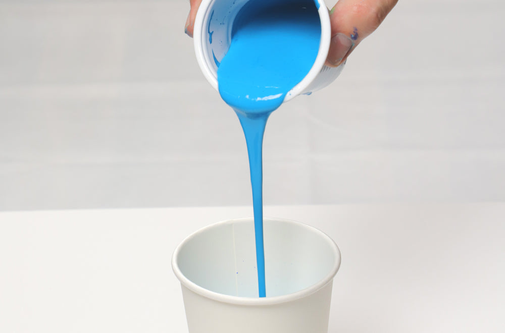Blue pouring paint being poured into cup.
