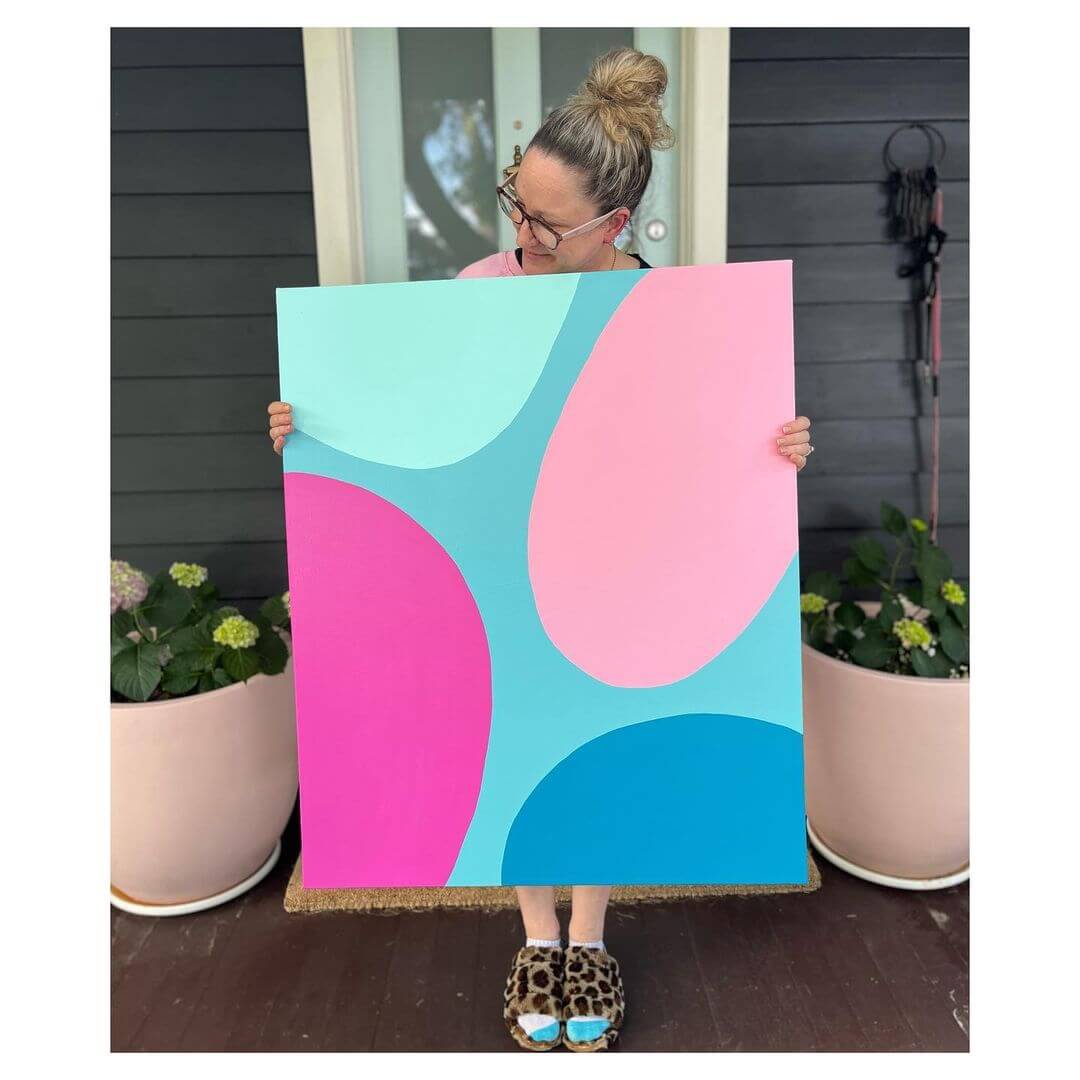 1. Artist Poppy Key holding a blue abstract artwork with blue and pink coloured ovals.