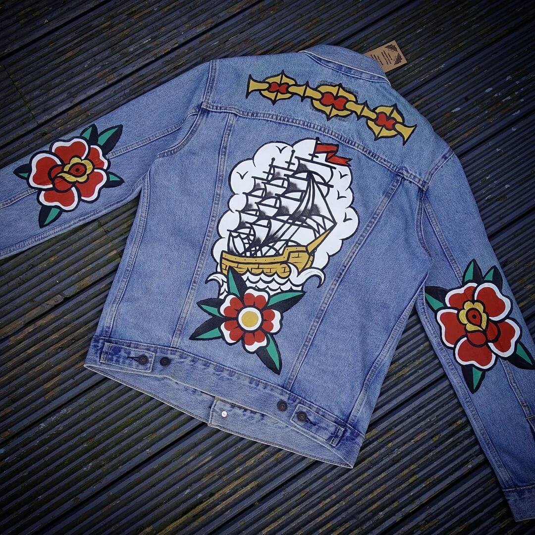 Denim jacket with traditional style tattoo art painted on the back.