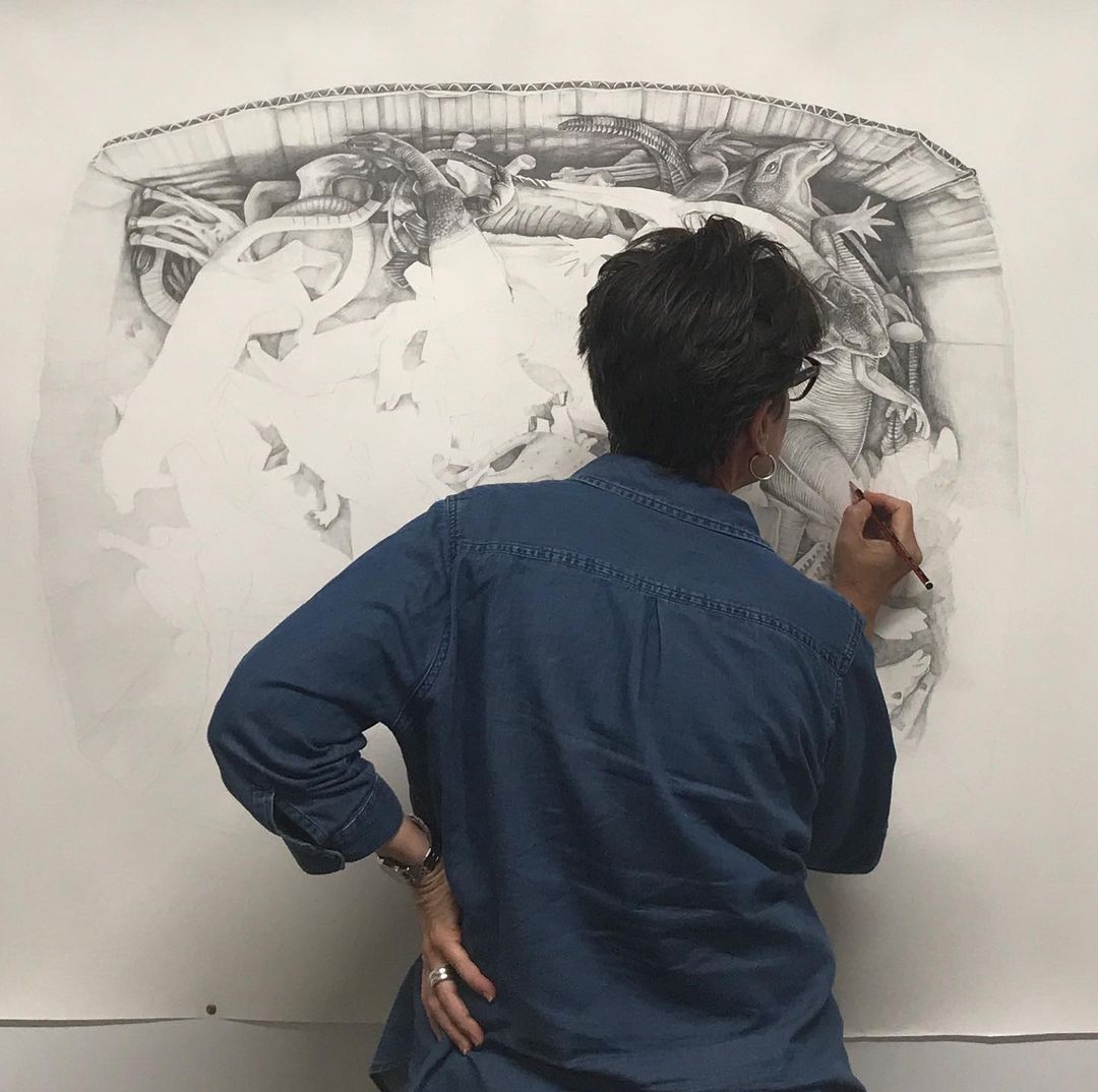 Kerry Daley sketching a large pencil drawing of toy figurines in a box