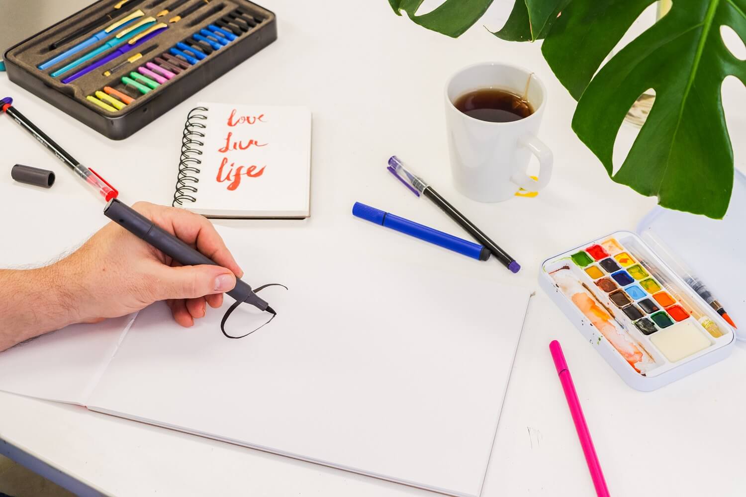 Left hand holding a brush lettering pen writing love life with purple ink in the underlining style.