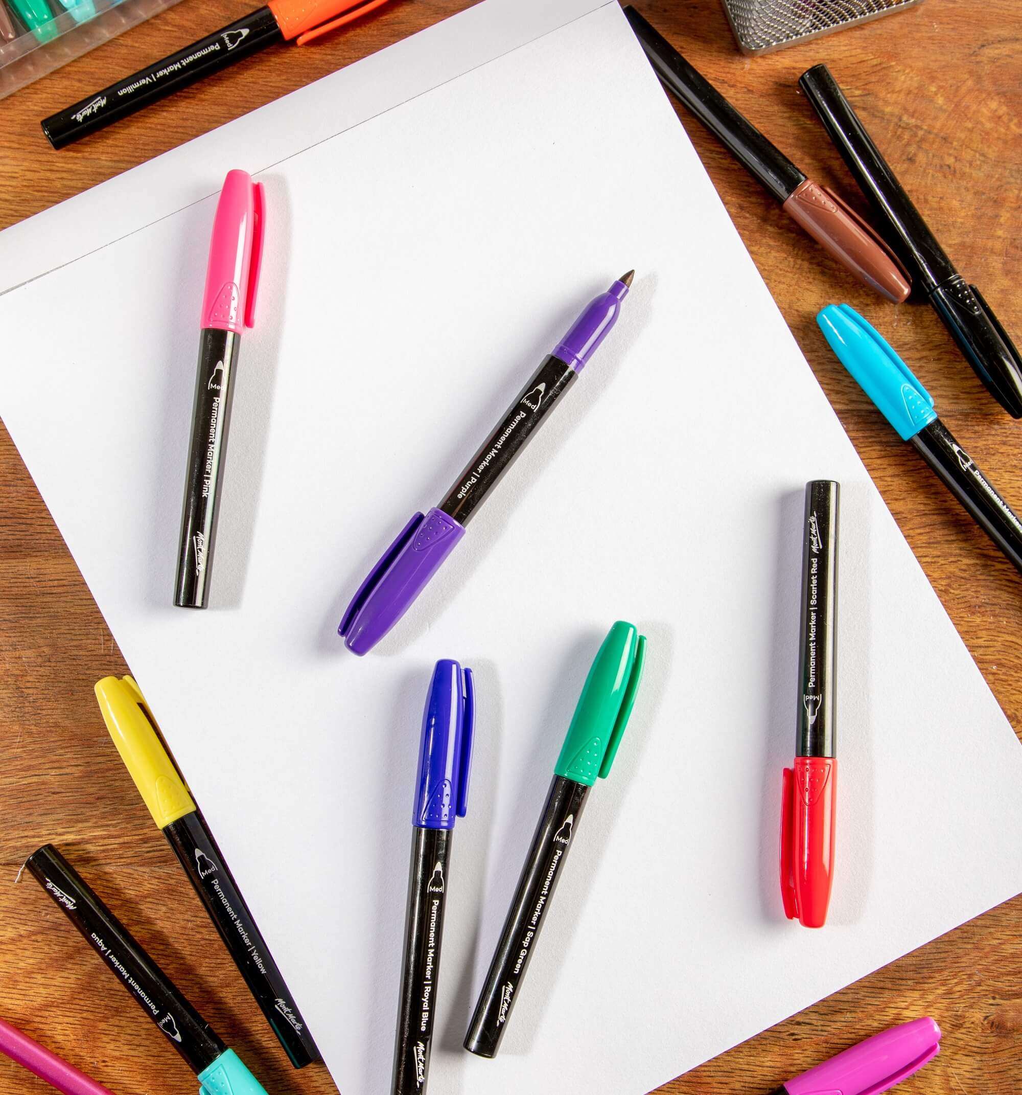 Lifestyle image of Mont Marte permanent markers lying on a white piece of paper on a timber desk.