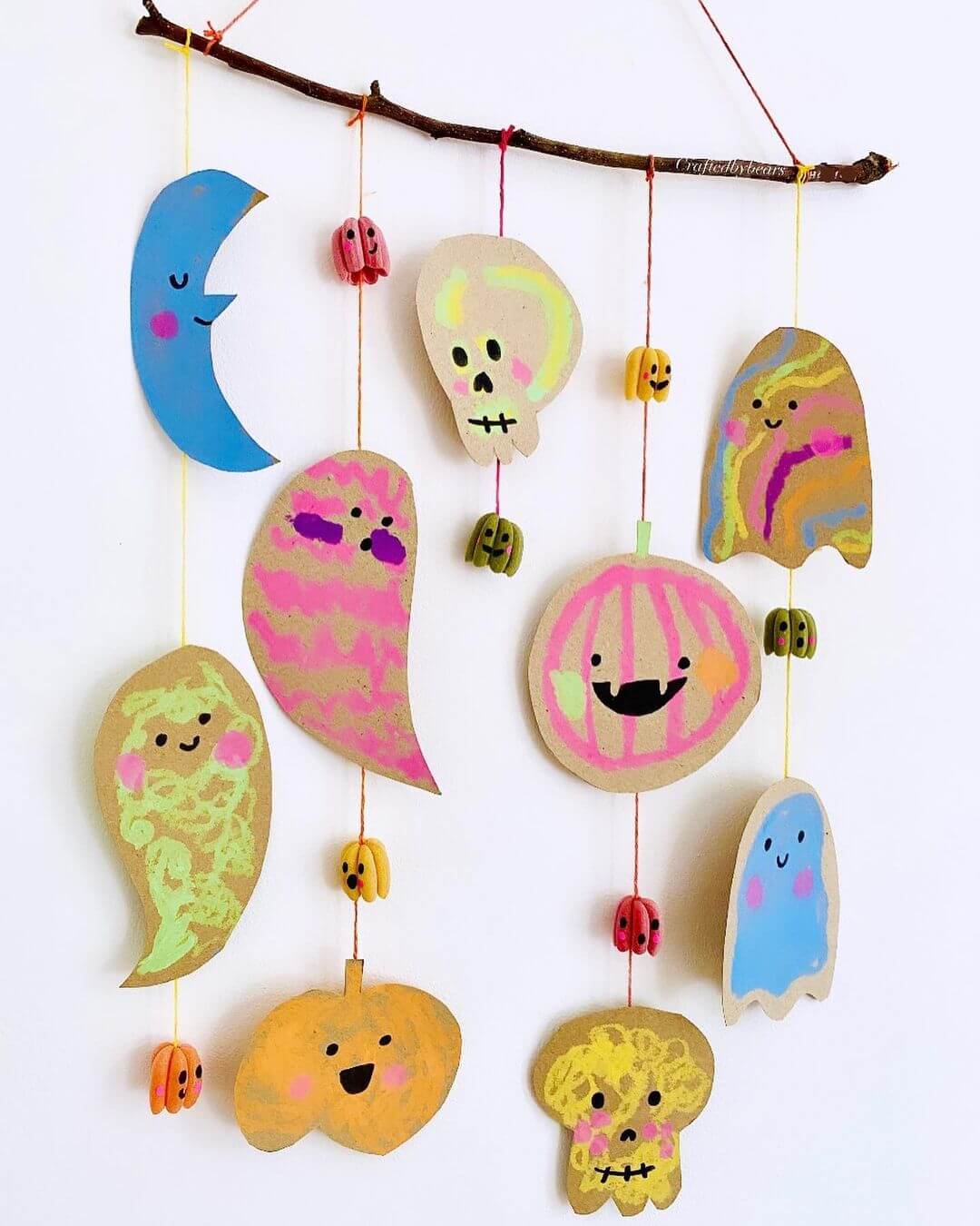 Pastel Halloween mobile made using cardboard, string and a branch. Ghosts, pumpkins, skeletons and a moon are made from pastel crayons and cardboard.