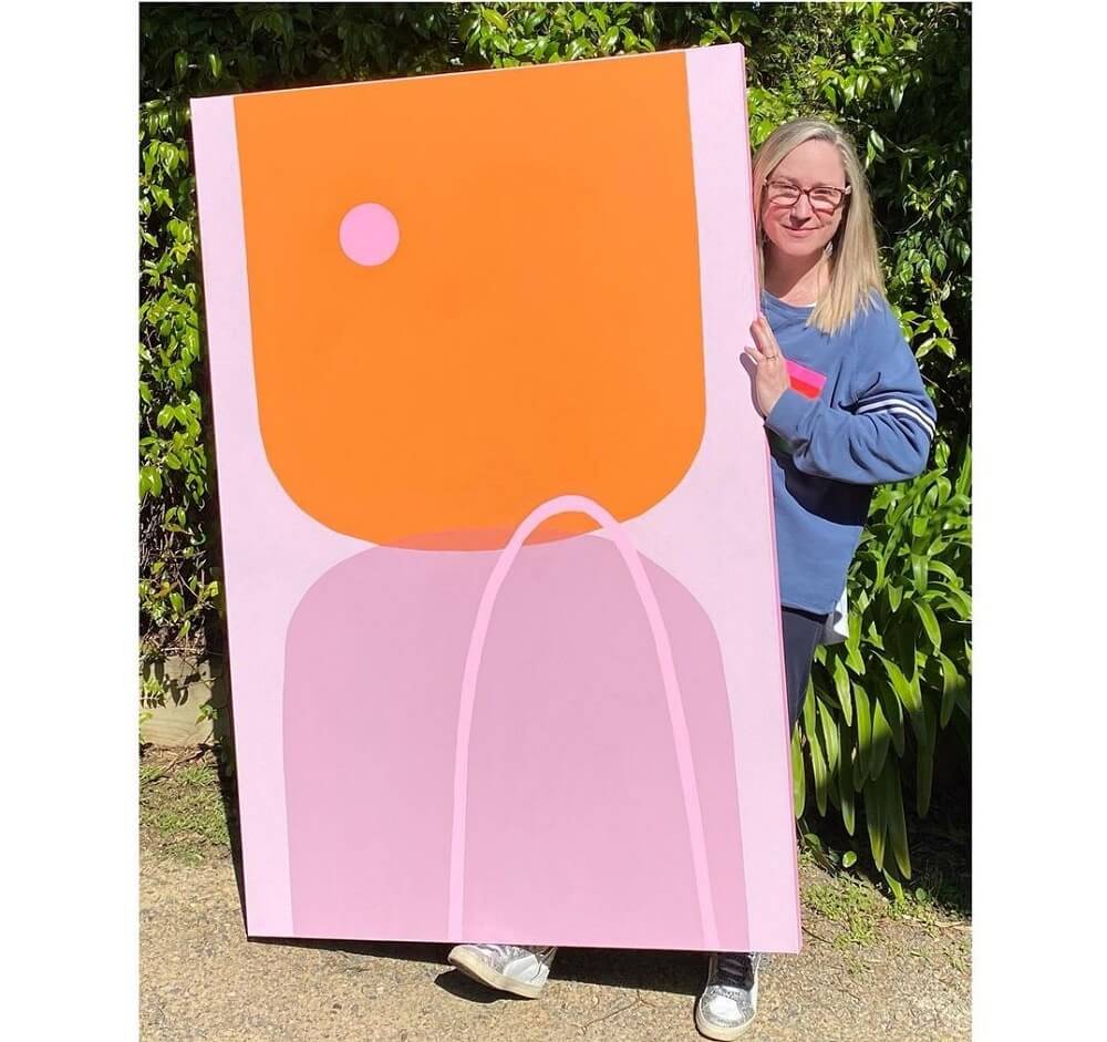 Poppy holding a large canvas with minimalist orange and pink abstract circles.