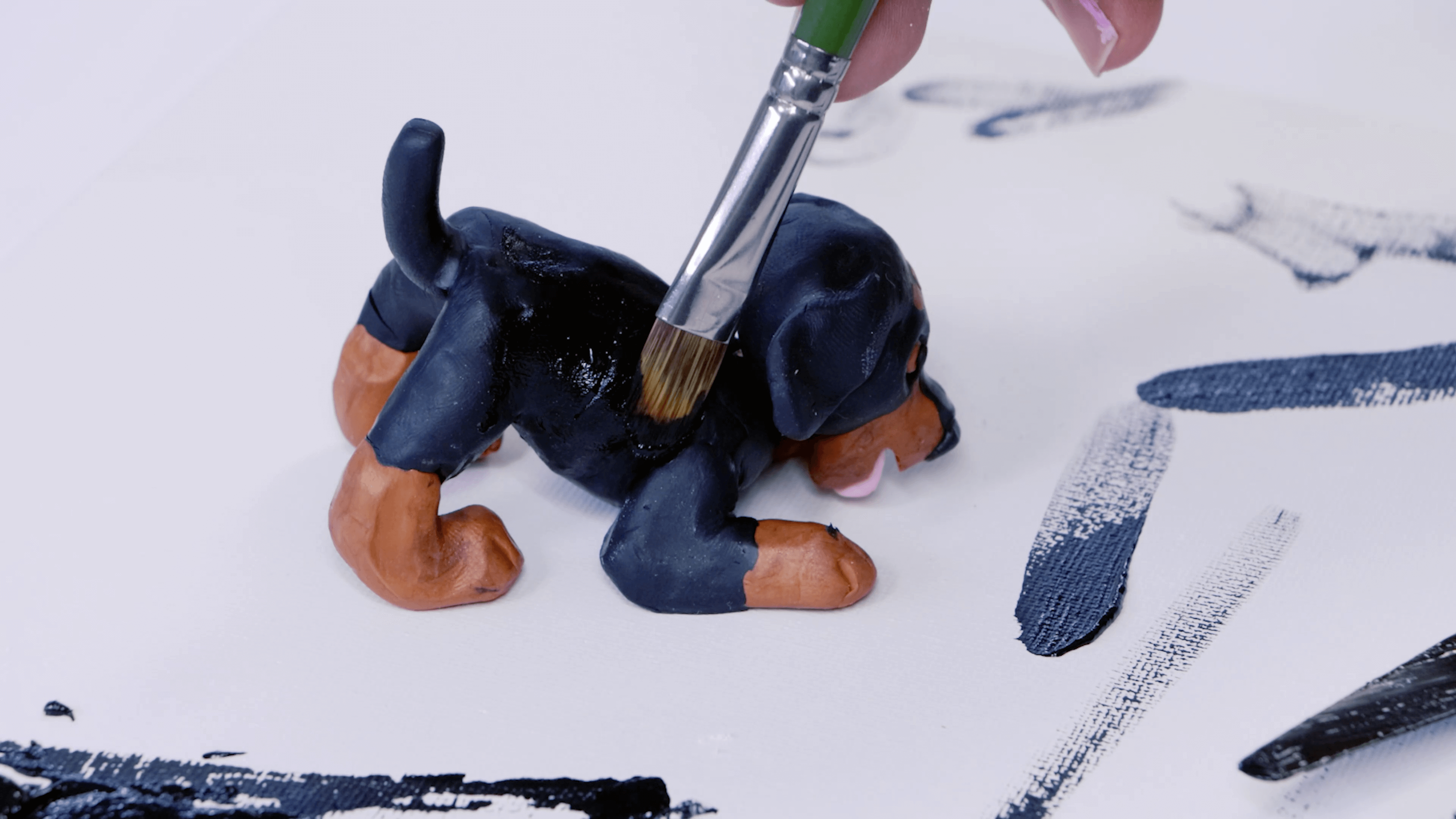 Brush paints over a black dog sculpture to hide cracks in the polymer clay.