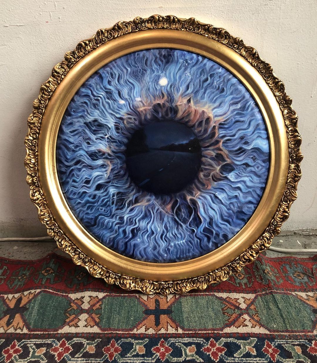 10. @edienadelhaft blue iris artwork framed in an ornate golden circle frame with a road reflected in the pupil