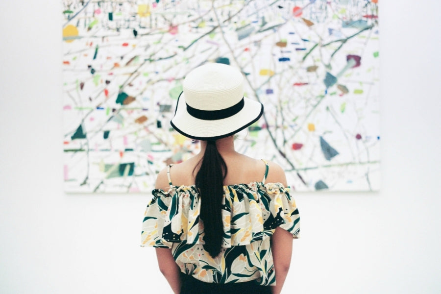 A woman wearing a white bowler hat standing in front of an art gallery.