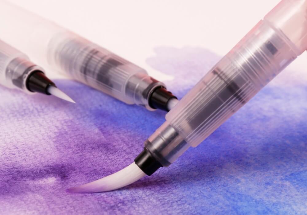 A watercolour water brush with purple colour laid onto paper.