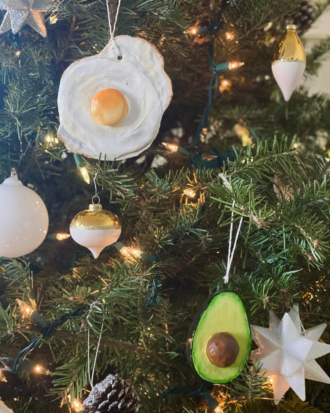 A fried egg and avocado Christmas decoration hanging from a Christmas tree amongst stars and baubles.