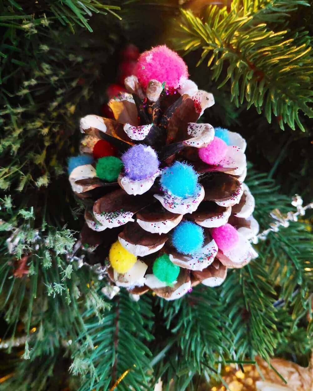 Brightly painted pinecone with pom poms glued.