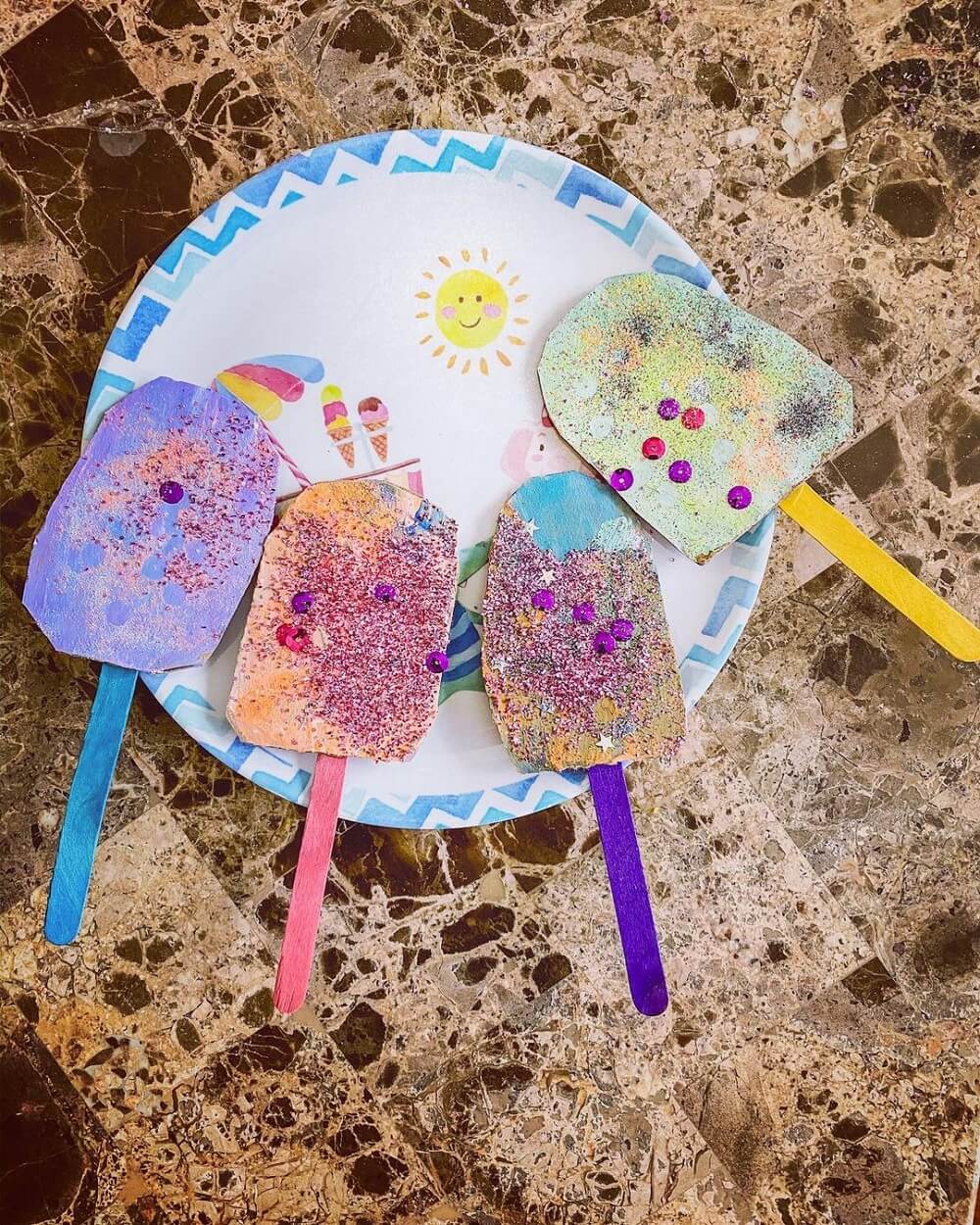 Four painted popsicles made from glitter and cardboard.