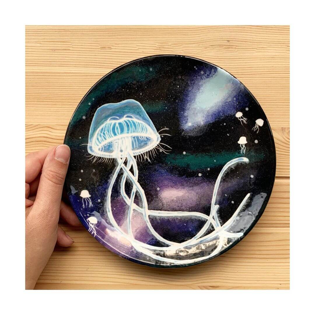 Hand holding a ceramic plate with jellyfish painted on it.