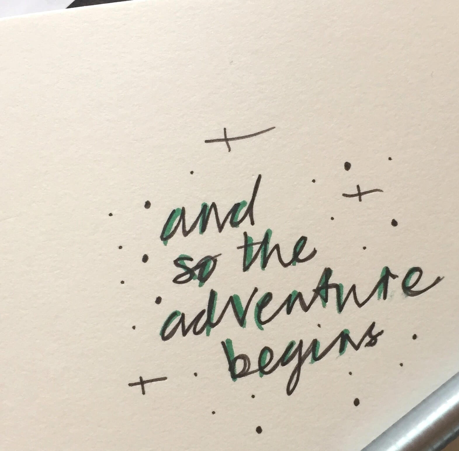 Hand lettering with two pens reading 'and so the adventure begins.'