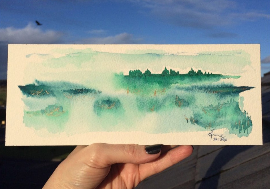 Hand holding a finished watercolour landscape.