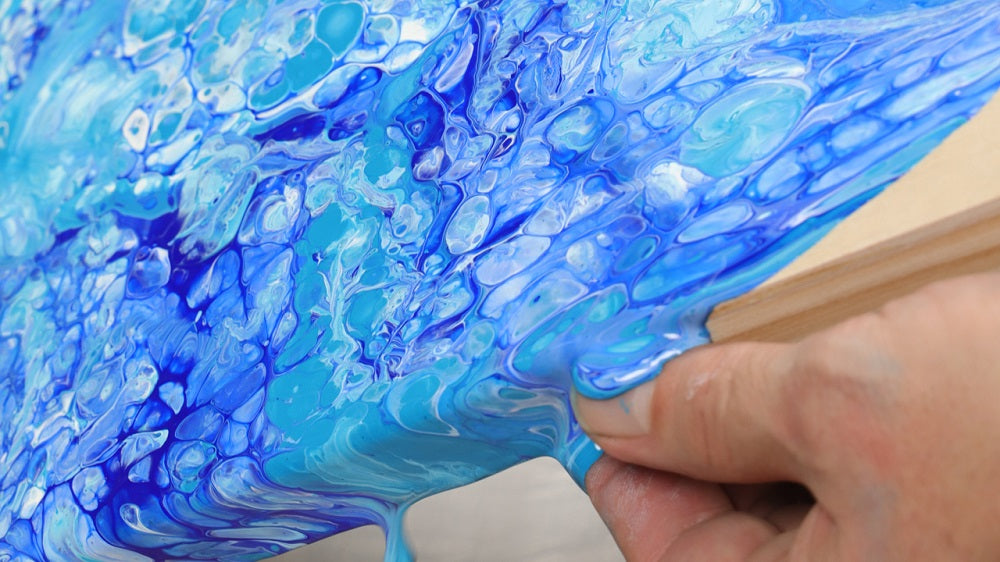 Light blue and dark blue pouring paint with a marble effect on a wooden panel.