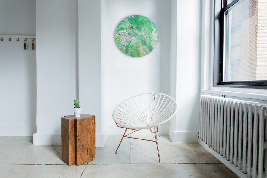 A green circular pour painting hanging on a wall.