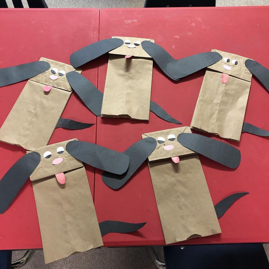 Five paper bag puppies made from craft paper and glued onto a paper bag to look like dogs.