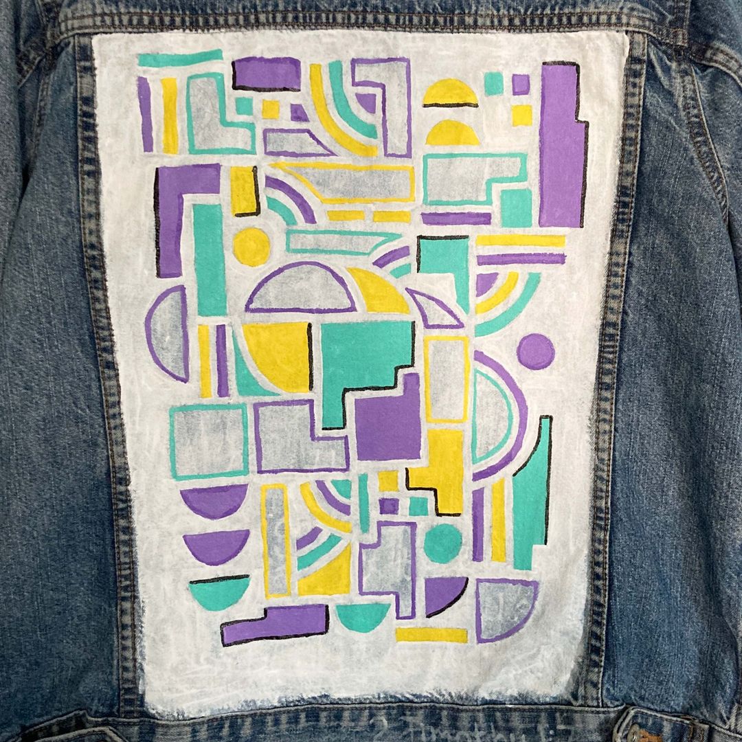 A geometric print painted in purple and yellow colours on the back of a blue denim jacket.