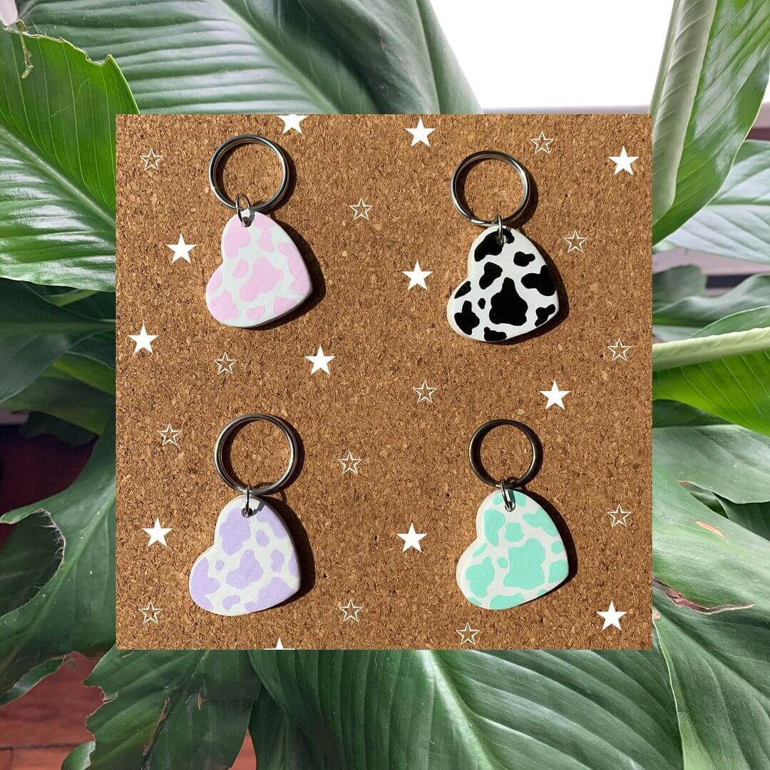 Four heart keyrings with coloured cow prints on a corkboard.