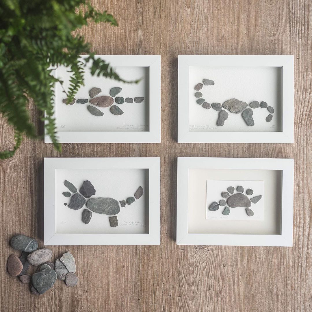 12. @thecookieraptor Four dinosaur pebble artworks in white frames with a fern in the top left corner